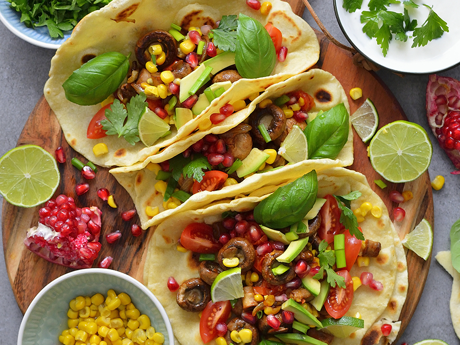Vegetarian tortilla tacos with tomato, corn and mushrooms, served on a wooden chopping board with sliced lime.