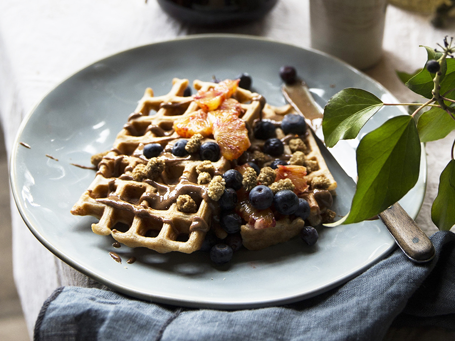 Vegan soy milk waffles served on a blue plate and topped with blueberries.