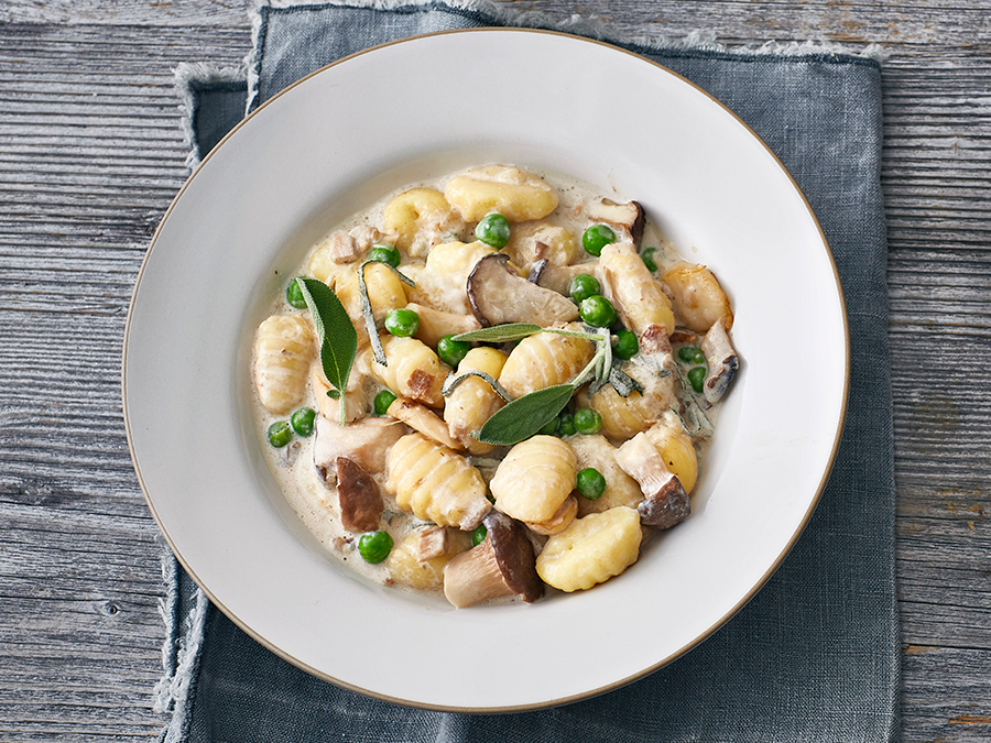Vegetarian gnocchi and mushroom ragout served in a white bowl on a grey wooden table. 