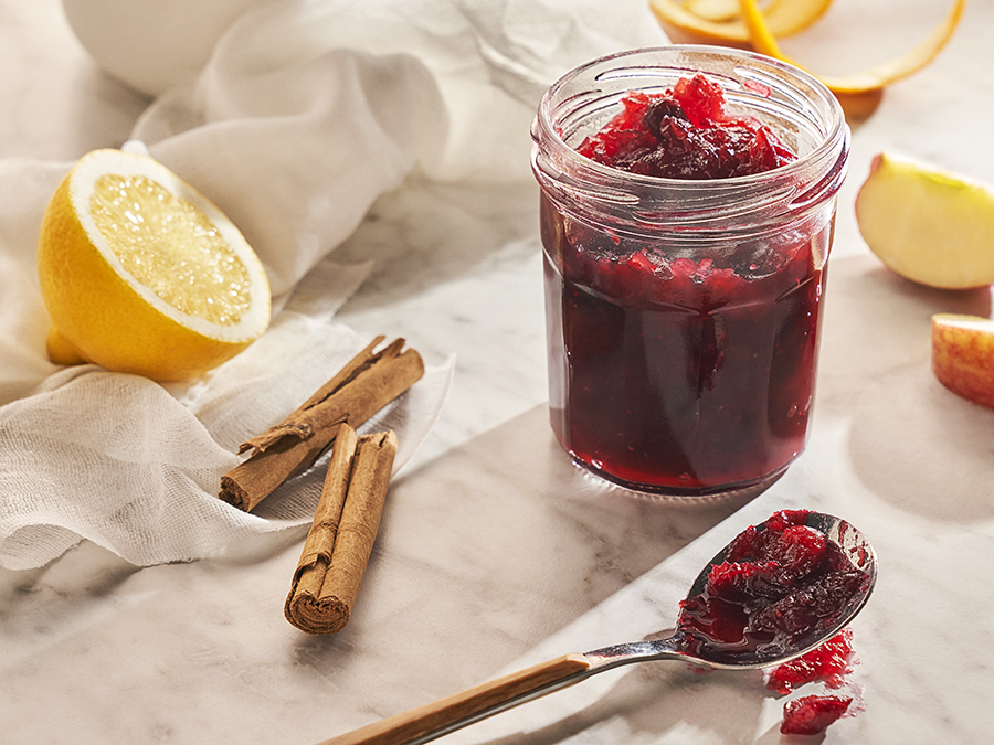 Cranberry jam in a glass mason jar surrounded by lemon wedges, and cinnamon sticks. 