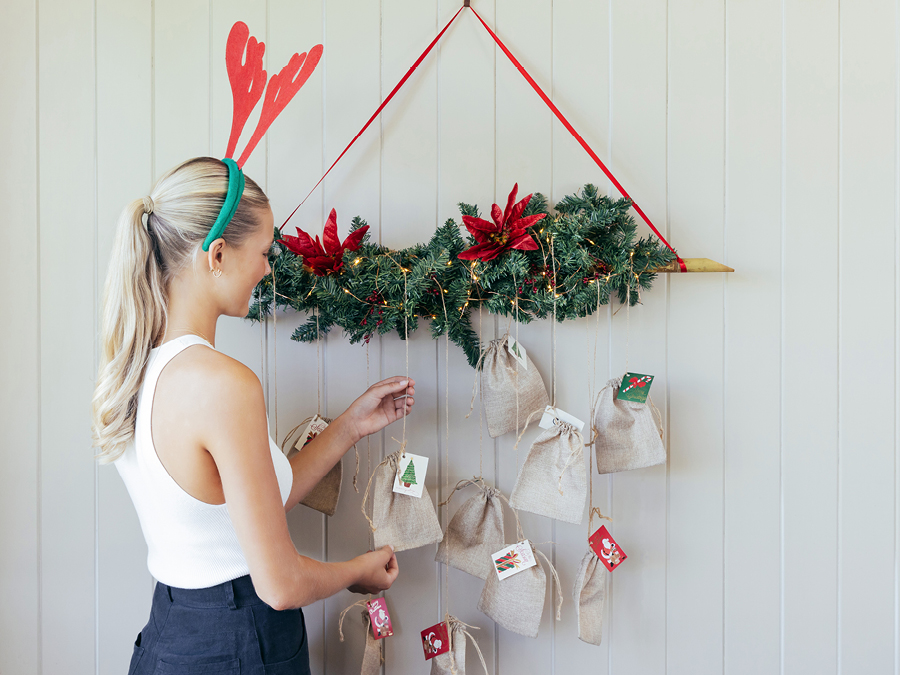 A young woman adding keepsakes and small gifts to a DIY Christmas advent calendar hanging on the wall.