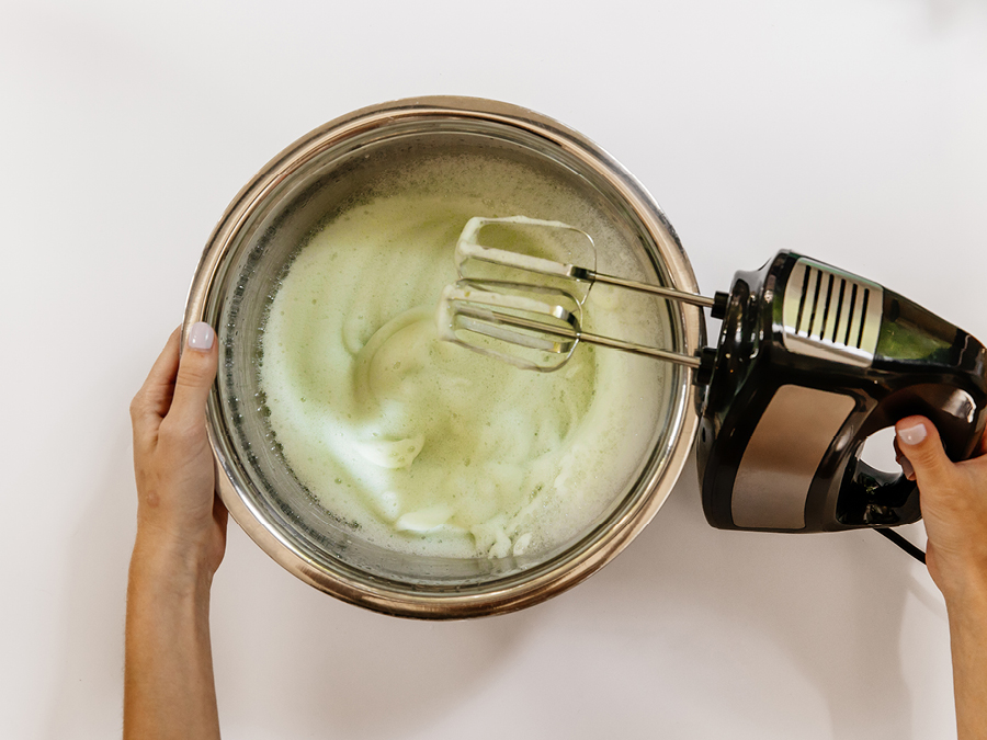 Green soap bubbles being mixed with electric mixer in a mixing bowl.
