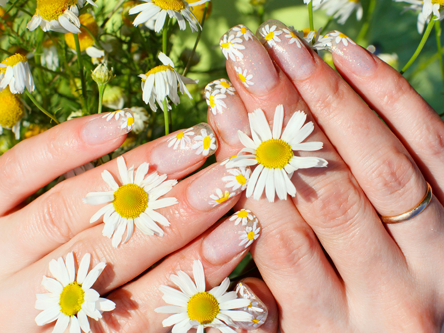 Hands displaying nail art with flowers between fingers. 
