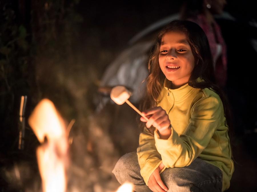 A girl toasting a marshmellow over an open fire.