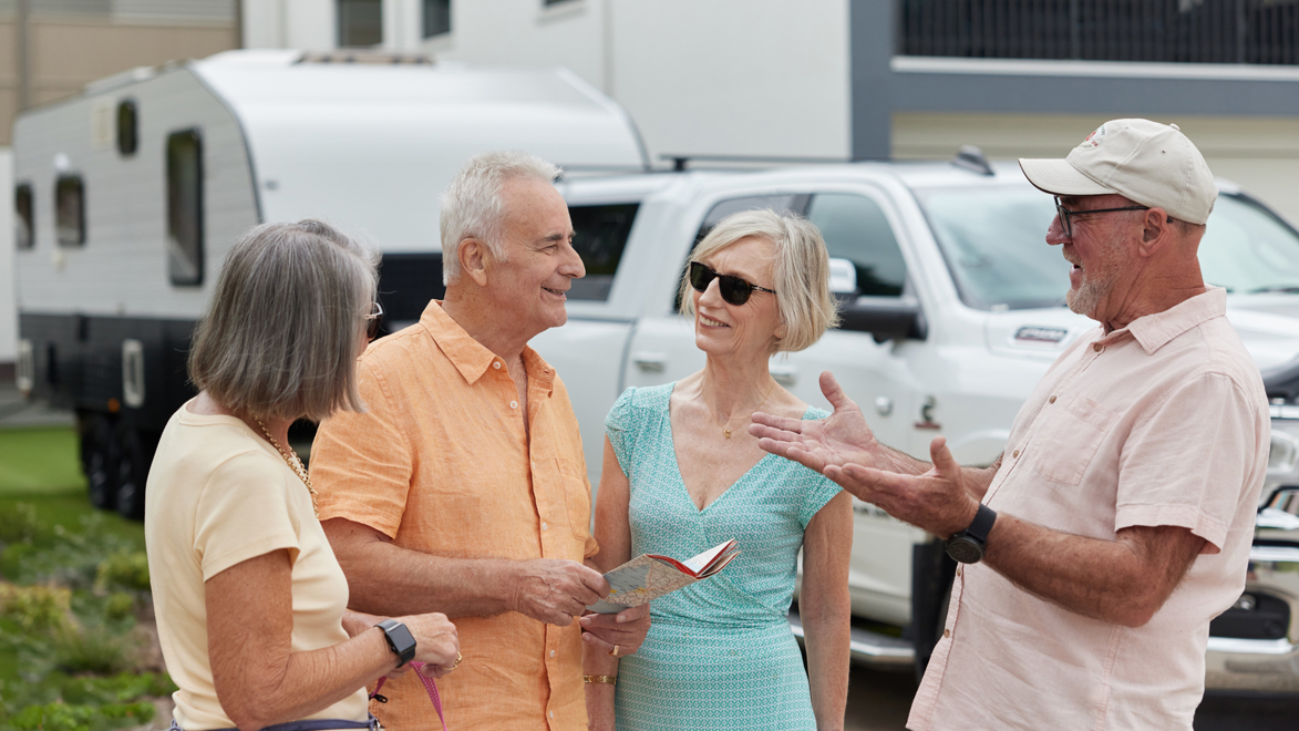 Friends chatting about their road trip with caravan packed and map for directions